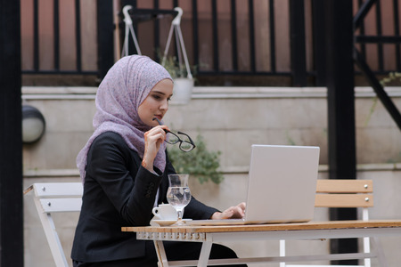 Young muslim girl typing on laptop and drink coffeeの写真素材