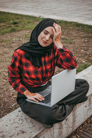 Young muslim girl typing on laptop and drink coffeeの写真素材