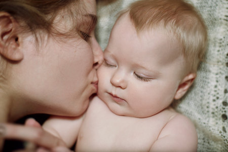 Close-up portrait of mother hugging and kissing her beautiful cute babの写真素材