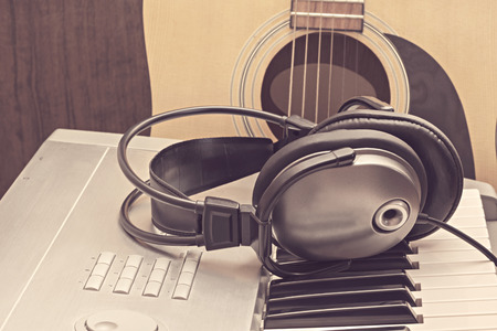 Digital midi keyboard, headphones and acoustic guitar in the studio.