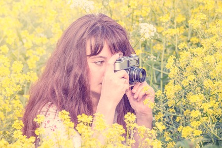 Woman shooting flowers on the meadow with vintage photo camera.の写真素材