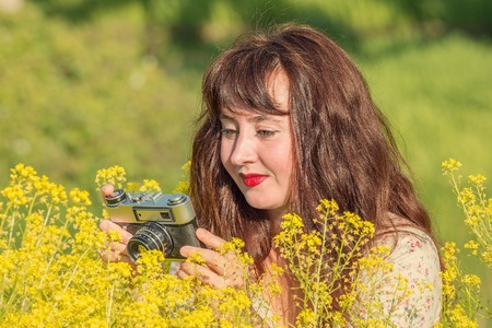 Woman shooting flowers on the meadow with vintage photo camera.の写真素材
