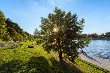 Moscow, Russia - August 22, 2015: People rest on the grass by the Moscow-river and tree at sunset time.のeditorial素材