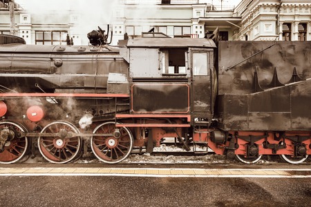 Retro steam train stands by the station building before departure.の写真素材