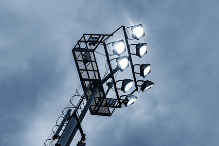 Stadium lights by the sports field on the cloudy sky background.