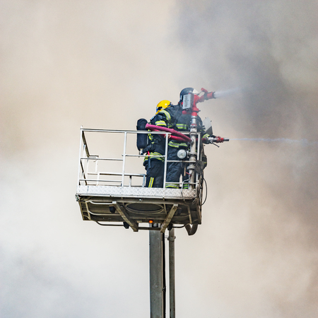 Firefighters extinguish a fire by the top of the building.の写真素材