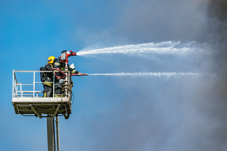 Firefighters extinguish a fire by the top of the building.の写真素材