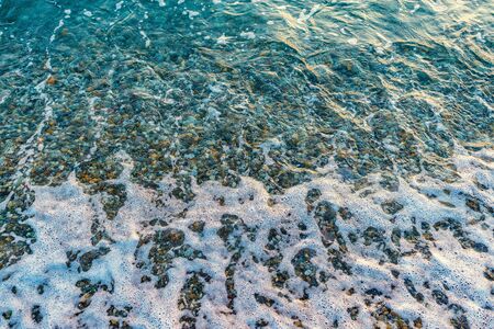 Small stones with sea wave on the beach at sunset time.の写真素材