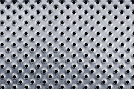 Close up of the silver colored metal background with holes.