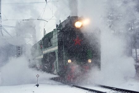 Retro steam train departs from the railway station at winter snowy time.