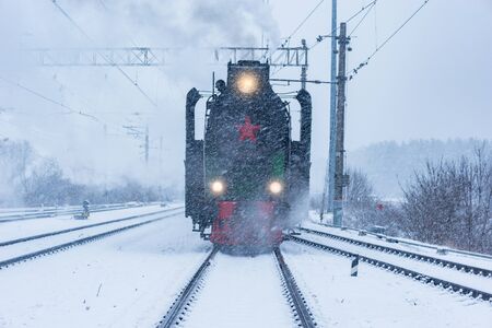 Retro steam train departs from the railway station at winter snowy time.