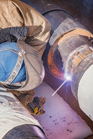 Welder worker welds new metal pipe on the construction site.