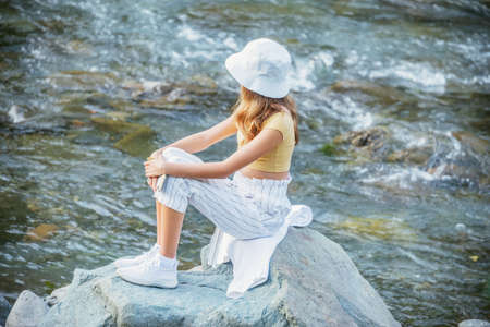 Young girl sits on the stone by the mountain river.の写真素材