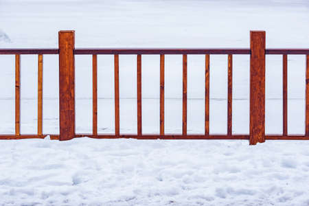 Wooden fence by the lake in the city park at winter time.