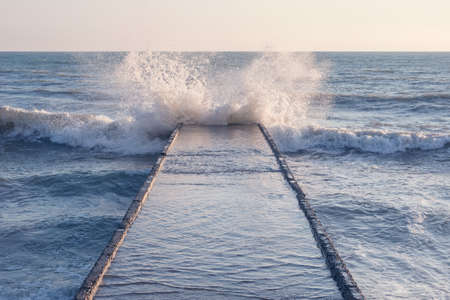Waves crash to the breakwater at stormy sunset time.の写真素材