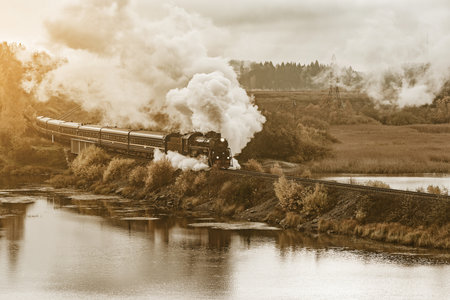 Retro steam train moves along the lake at autumn cloudy morning. Republic of Karelia. Russia.の写真素材
