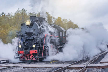 Retro steam train departs from the station wooden platform at cloudy autumn evening.の写真素材