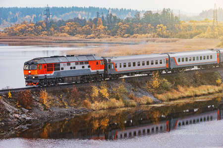 Passenger train moves along the lake at autumn morning. Karelia. Russia.の写真素材