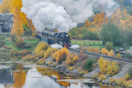 Retro steam train moves along the lake at autumn cloudy day. Karelia.の写真素材