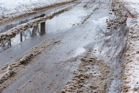 Melting snow and puddles on the road at early spring.の写真素材