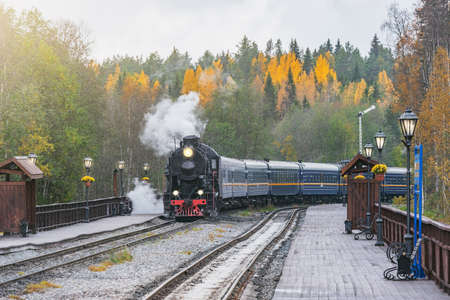 Retro steam train arrives to the station wooden platform. Ruskeala Mountain Park. Republic of Karelia.の写真素材
