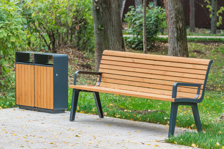 Bin for waste collection and wooden bench in the city park.の写真素材