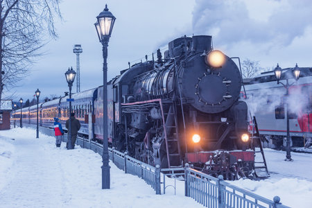 Retro steam train arrives to the station platform at winter evening.の写真素材