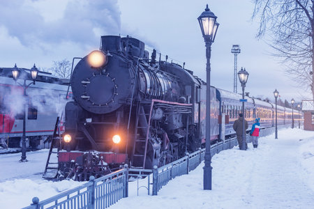 Retro steam train arrives to the station platform at winter evening.の写真素材