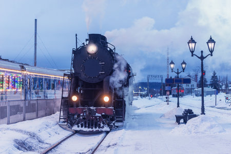 Retro steam locomotive stands by the station platform at winter evening.の写真素材