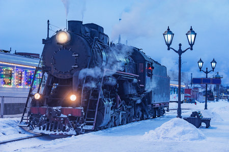 Retro steam locomotive stands by the station platform at winter evening.の写真素材