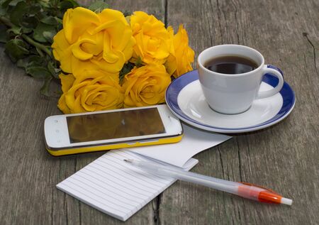 cup of coffee, phone, bouquet of roses and notebook with the handleの写真素材