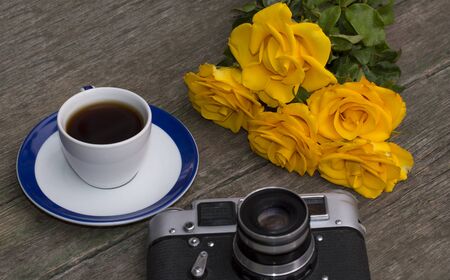 the old film camera, roses and coffee on a wooden tableの写真素材