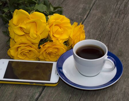 coffee, yellow roses and the mobile phone on a wooden tableの写真素材