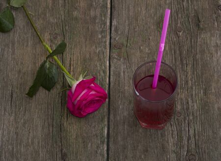 glass of juice and lonely red rose on a tableの写真素材