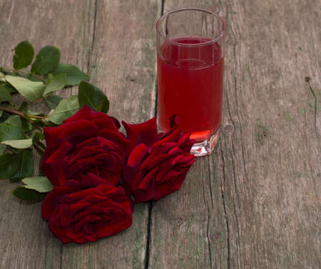red glass of juice and bouquet of red rosesの写真素材