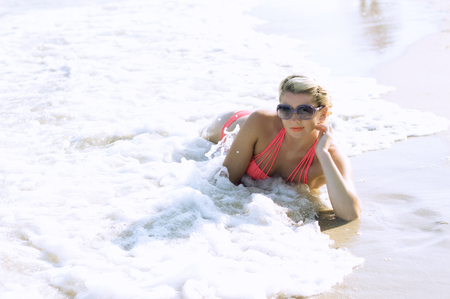 the beautiful woman in orange bikini lies in a penalty fee of sea waves, a subject sea tourの写真素材