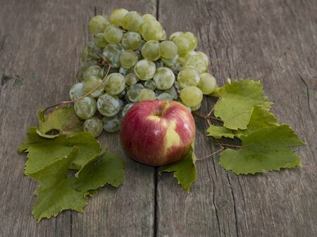 apple and cluster of grapes with leaves on a wooden table, a still life on a subject fruit of fallの写真素材