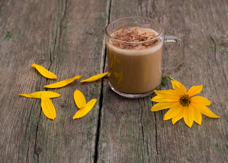 transparent mug with a cappuccino, a yellow flower and petals, a still life, on a wooden table, a subject flowers and drinksの写真素材