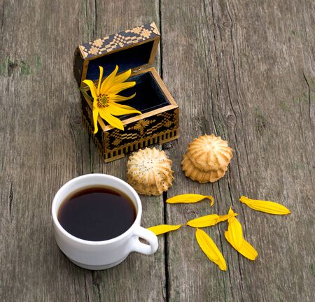 cup of coffee, open casket with a flower, two linking of cookies and petals, a still life on an old table, a subject food and drinksの写真素材