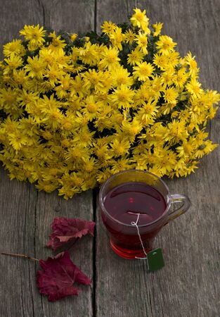 still life, bouquet of yellow flowers, transparent cup of tea and red leaf, on a wooden table, fall, a subject drinksの写真素材