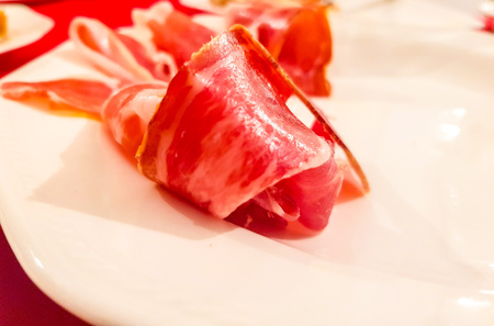 Piece of Serrano ham on a white background. You can appreciate the reddish color and the typical fat streaks. Ham on a plate on a white background.の写真素材