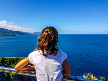 girl with her back to the blue sea leaning on a chromed railing. Unrecognizable girlのeditorial素材