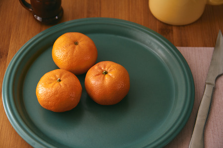 Mandarins. Close-up of tangerines on a plate and with table elements such as cup and cutlery. wooden back. Mandarin backgroundの写真素材