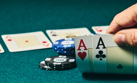 close-up of two aces held in one hand on the green game mat on the right side of the image to leave...