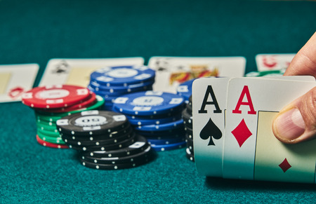 close-up of two aces held in one hand on the green game mat on the right side of the image to leave room for editing, other cards and poker chips are on the matの写真素材