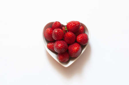 Strawberries, top view of sweet and delicious red strawberries in heart shaped bowl, isolated on white background. Selective focus.の写真素材
