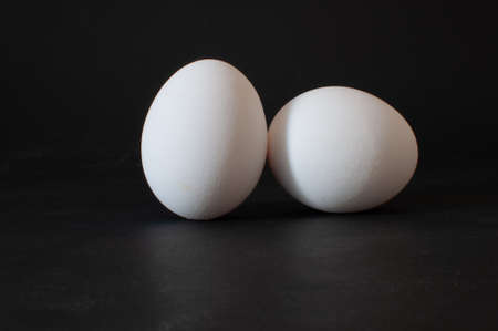 Two eggs, profile view of white raw chicken eggs isolated on dark background, selective focus.の写真素材