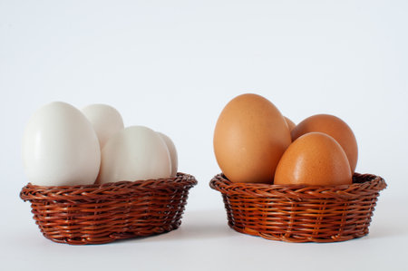 Brown and white chicken eggs in brown color mini baskets, isolated on white background. Don't put all your eggs in one basket idea concept.の写真素材
