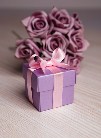 violet roses and gift box with pink ribbon on wooden surfaceの写真素材