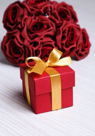 red roses and red gift box with yellow ribbon on wooden surfaceの写真素材
